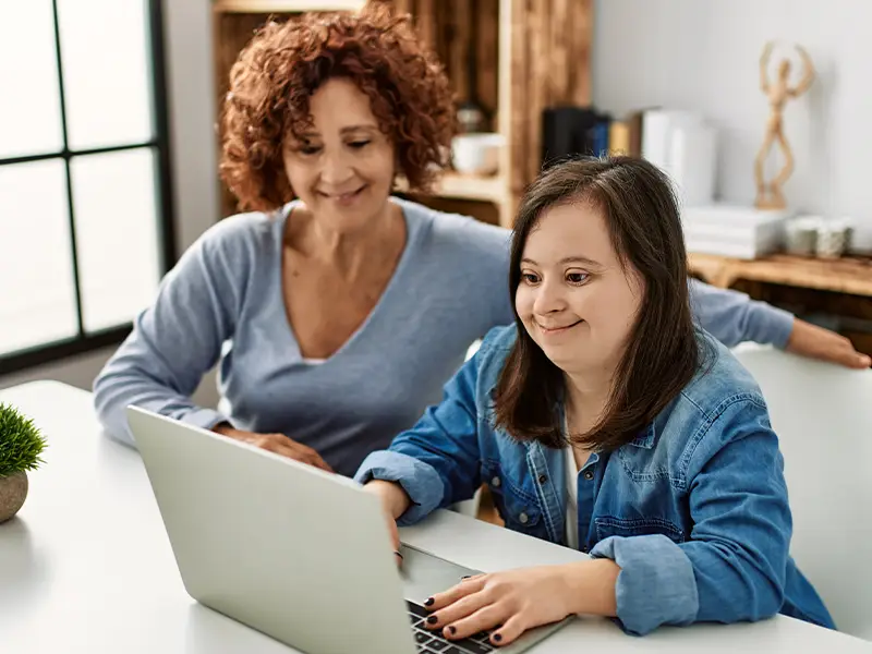 Mother and special needs daughter using computer laptop at home to apply