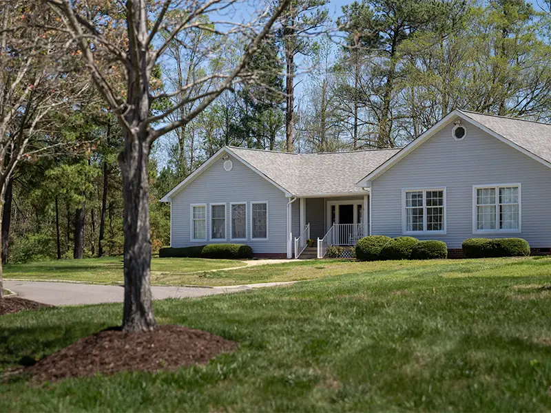 peaceful view of cottage surrounded by woods, walkway, grass