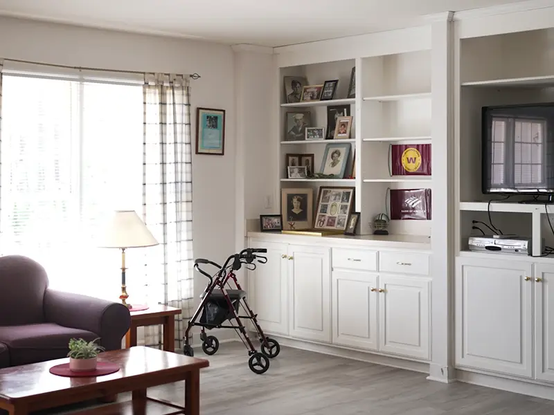 Living area with bright natural light,  white bookcases and sofa, walker, coffee table