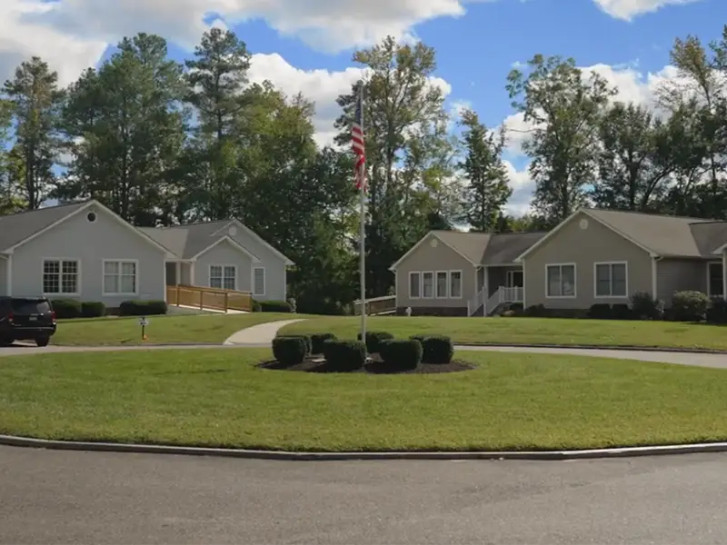 Exterior of grounds with Remington and Anne Carter Robins cottages in the background surrounded with a back yard of tall trees
