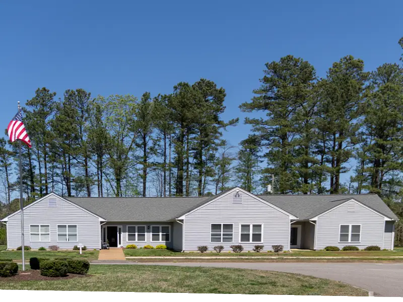 Founders cottage exterior, landscaped, surrounded by large trees, circular road, American flag and walkway
