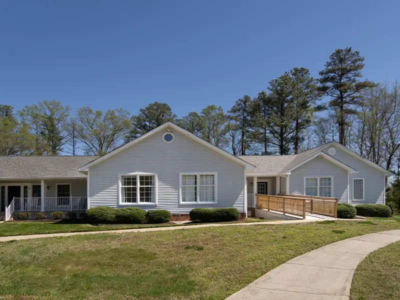 Remington cottage exterior with grass and walkway. Large trees in the background